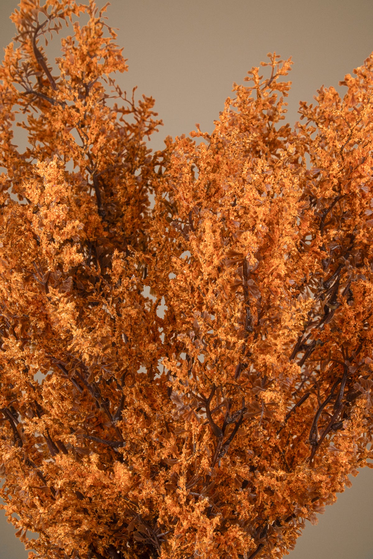 Artificial autumn foliage with dense orange-brown leaves and dark branches, photographed against a plain warm gray background.