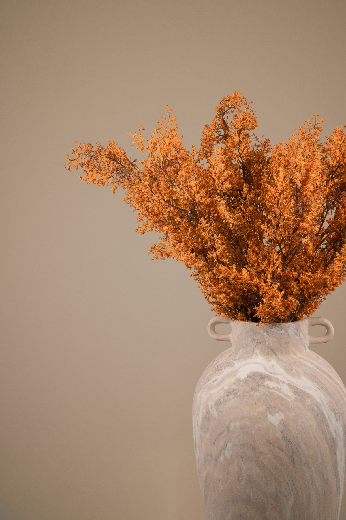Dried orange foliage arranged in a textured off-white ceramic vase against a solid warm beige background.