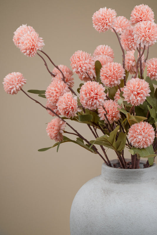 Pink pom-pom dahlia artificial flowers arranged in a textured light gray ceramic vase against a solid beige background.